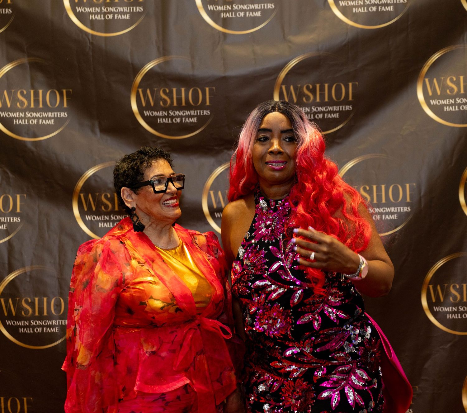 Two women pose at the WSHOF Women Songwriters Hall of Fame event backdrop.