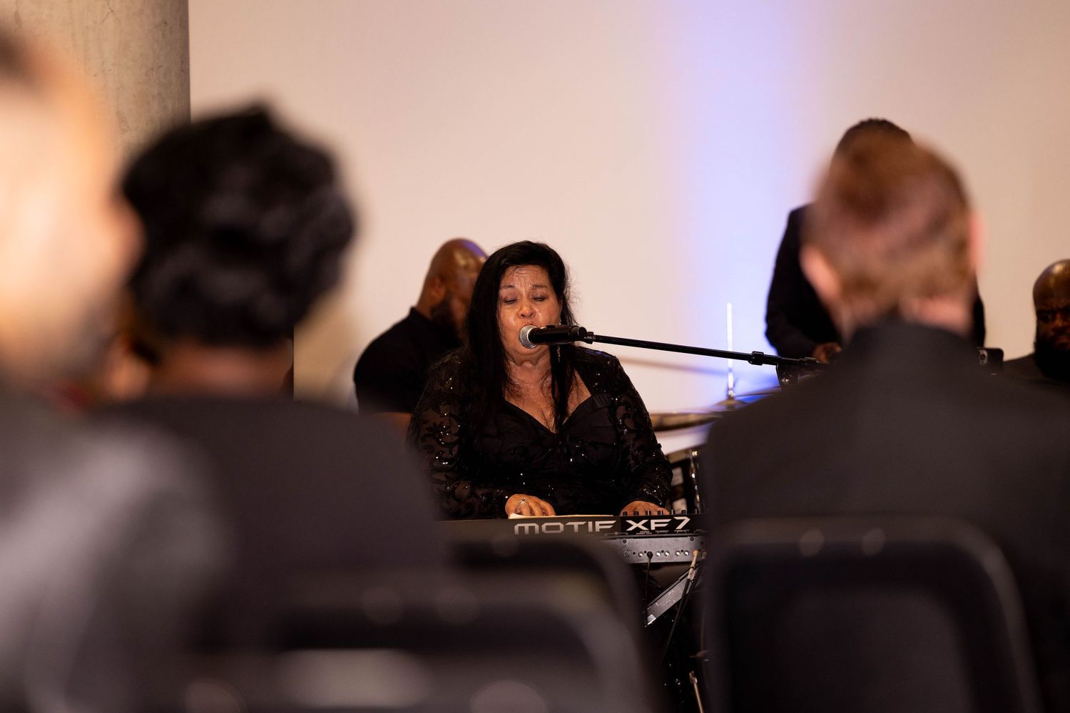 Female musician singing and playing keyboard at formal indoor event in black attire.