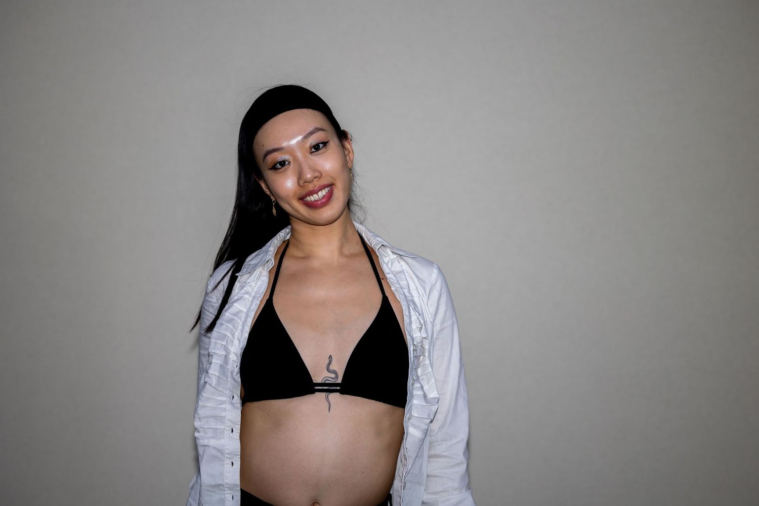 A smiling Asian woman in a black bikini top and white jacket poses against a neutral background.