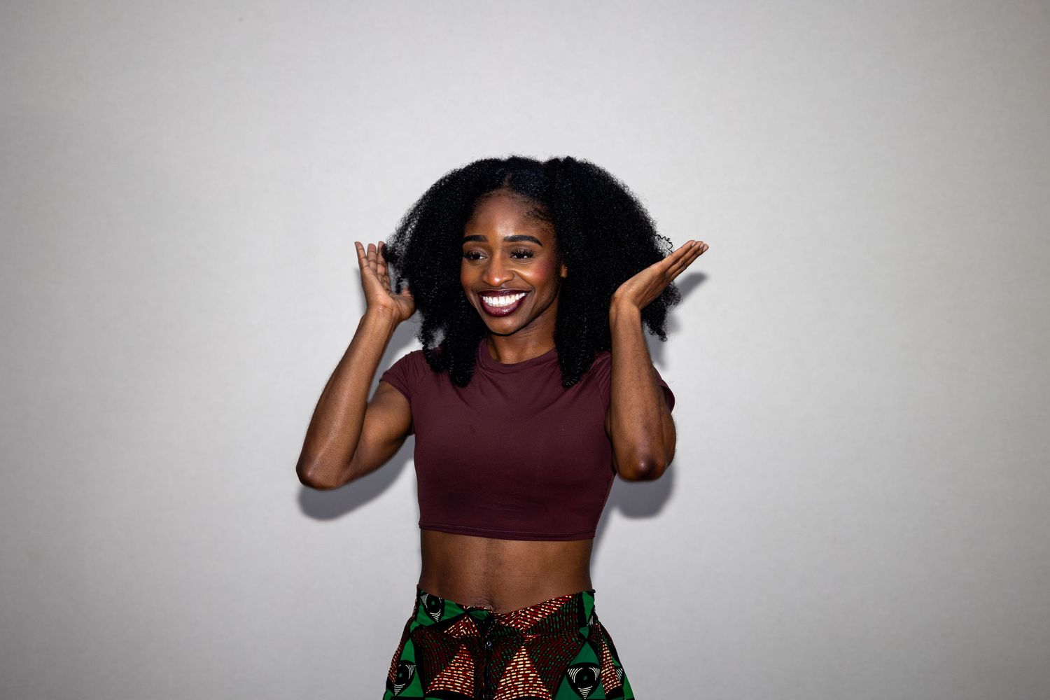 Joyful Black woman with natural hair laughing in a maroon crop top and vibrant printed skirt.