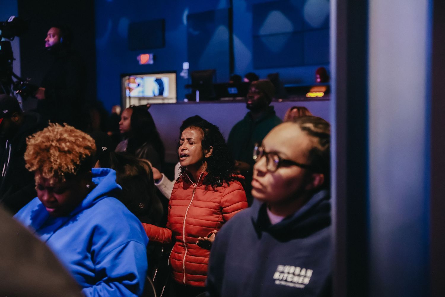A crowd of people wearing blue and orange jackets gather in a dimly lit indoor space.