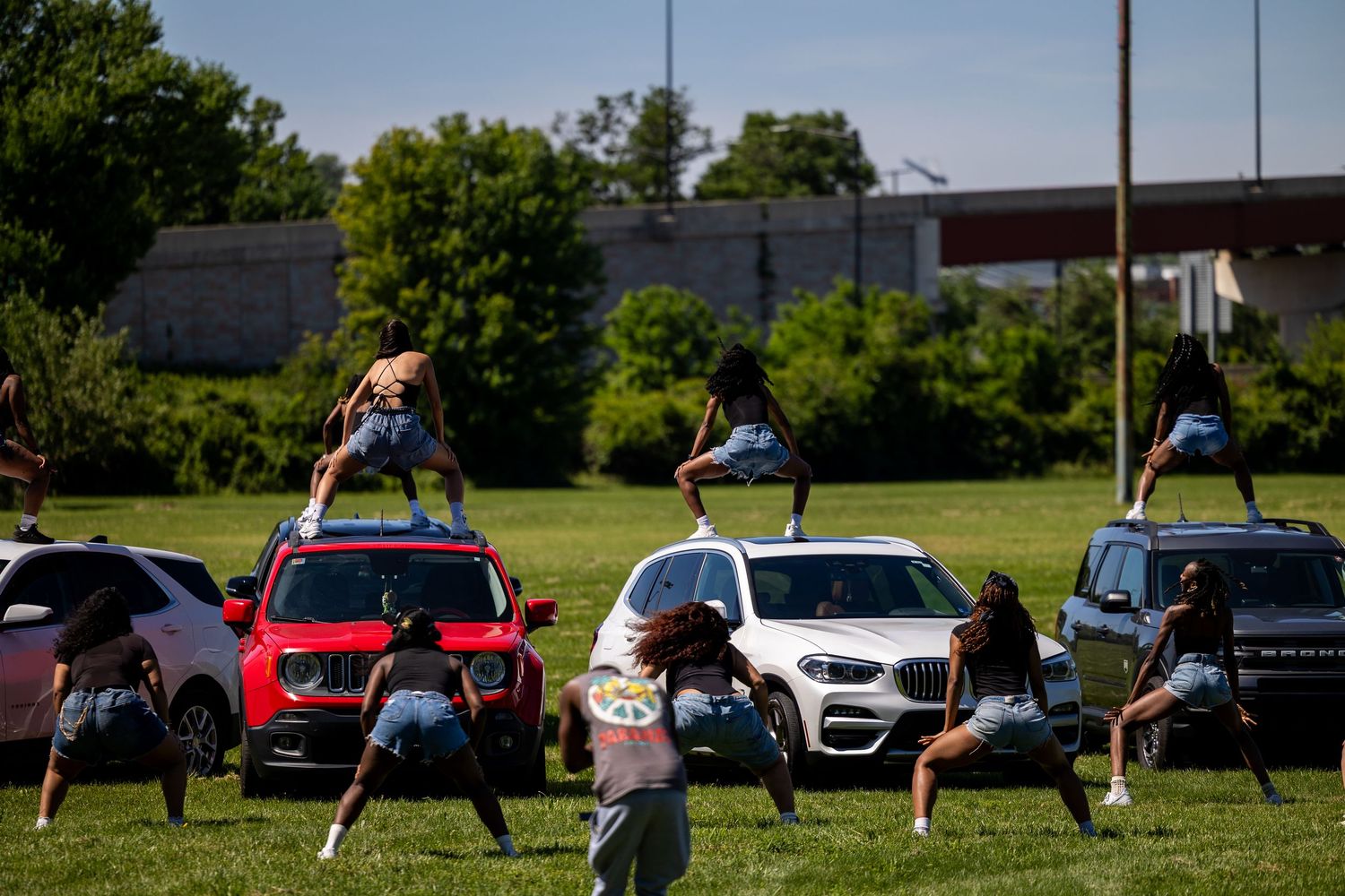 Cheerleaders performing energetic dance routines on cars at an outdoor event on a sunny day.