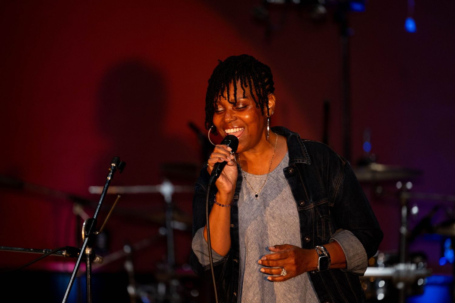 Woman singing into microphone on stage with dramatic red and blue lighting at a live music event.