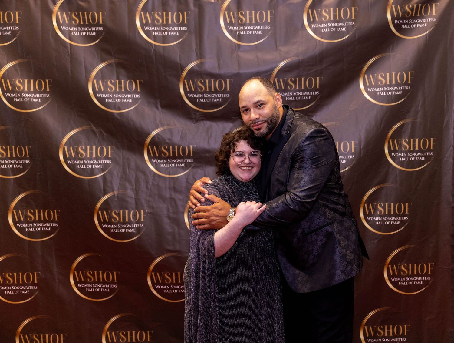 Two people posing together at a WSHOF event backdrop, sharing a warm embrace in formal attire.