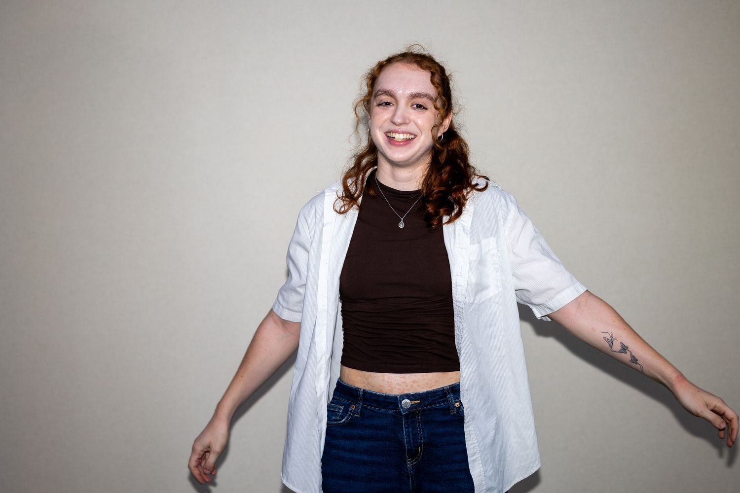 Cheerful young woman with curly hair in a white open shirt and black crop top spreading her arms.