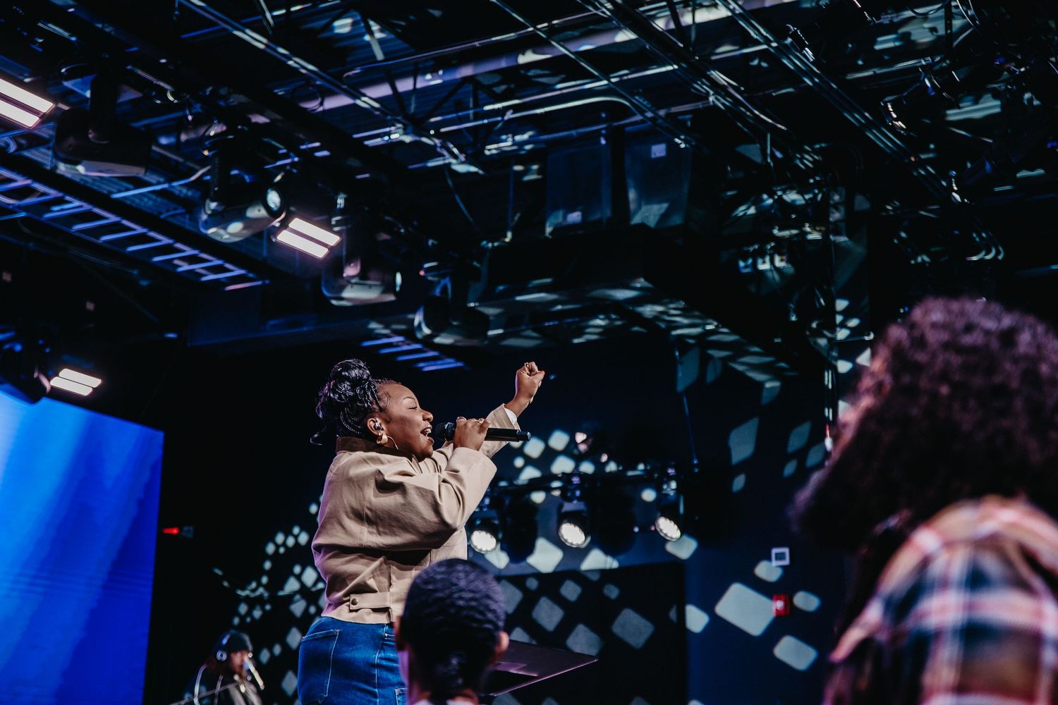 A performer sings passionately on stage with dramatic blue lighting and silhouetted audience members in the background.