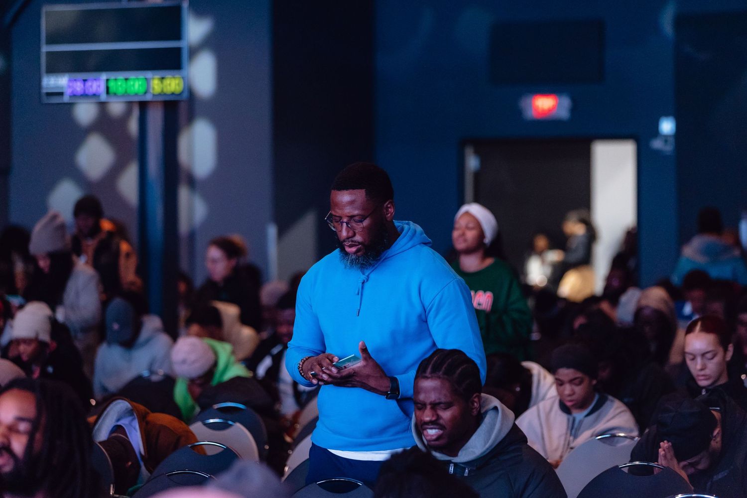 A person in a bright blue shirt stands in front of a crowd at an indoor event venue.
