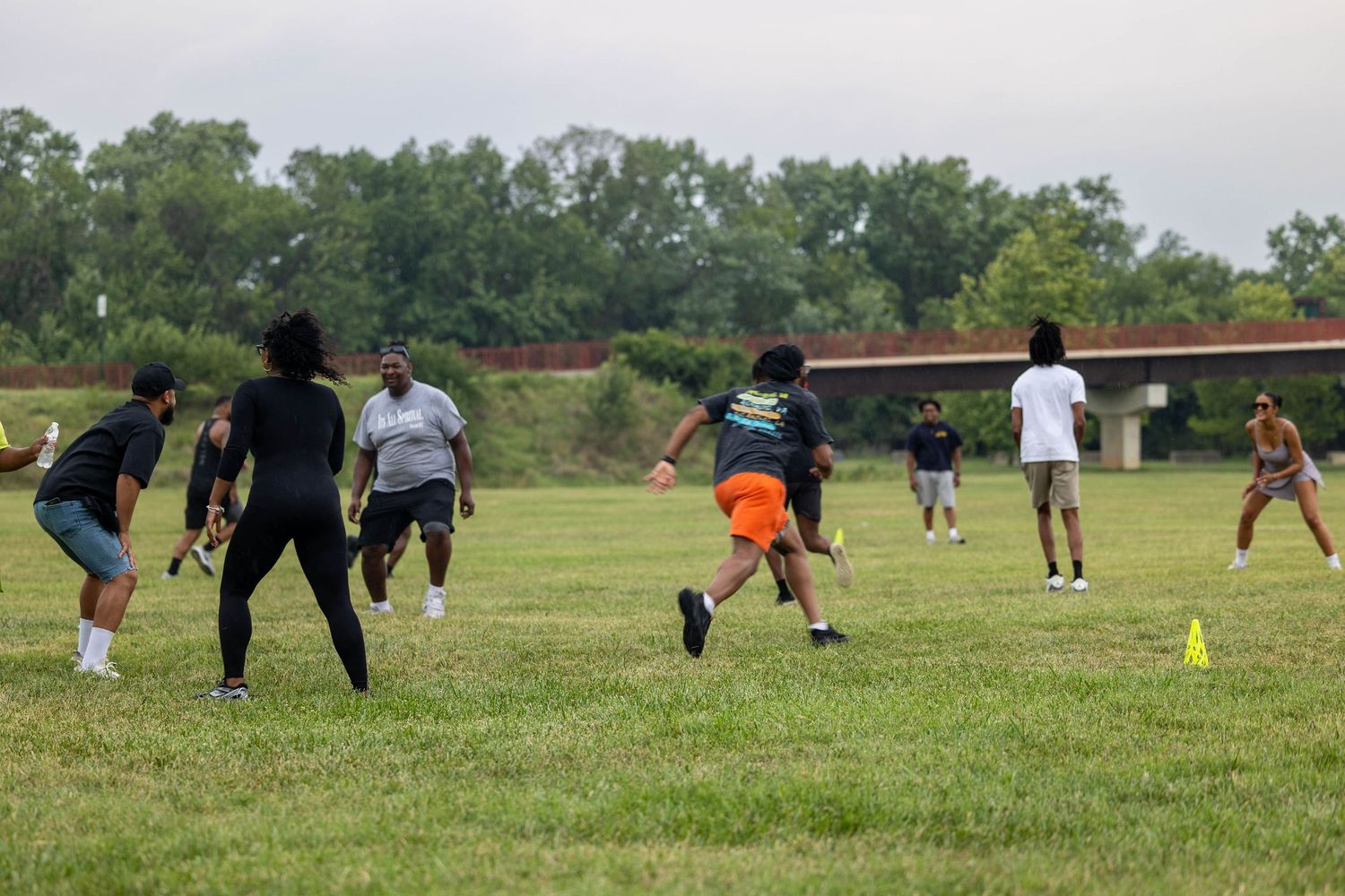 Group of people playing flag football on a green grass field outdoors on a cloudy day.