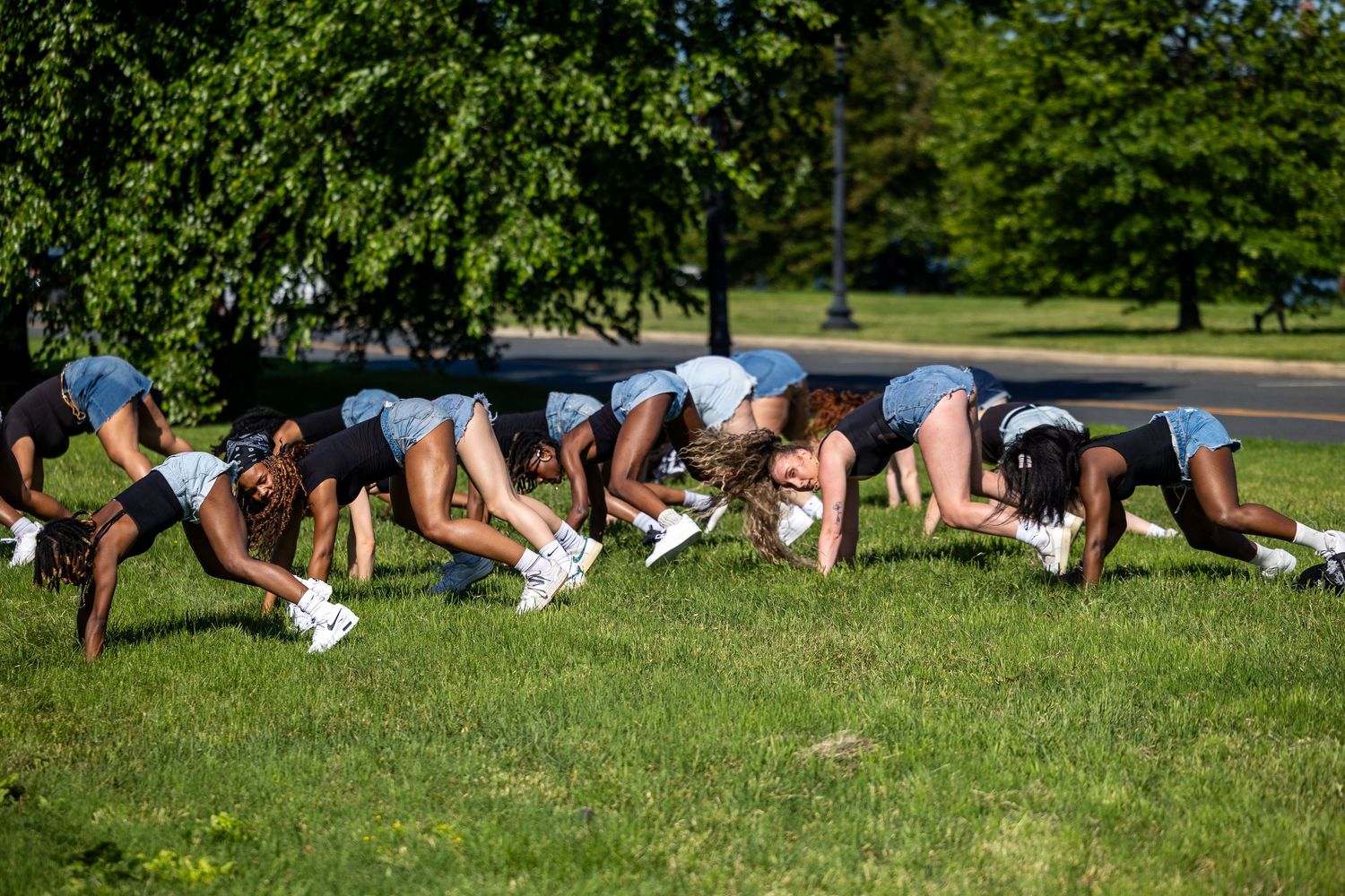 Group of cheerleaders practicing backbends on green grass in a sunny park setting.