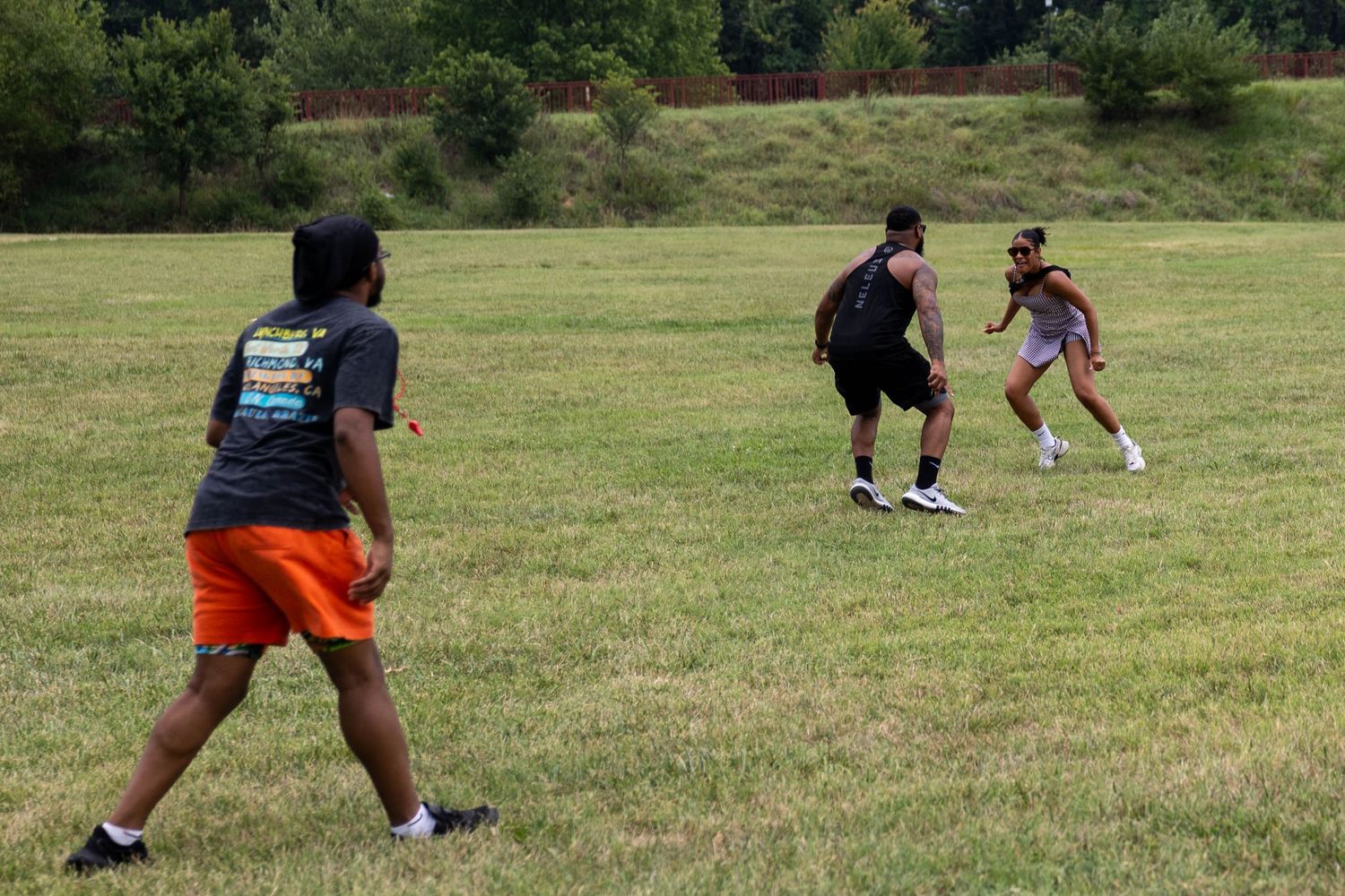 Group of people playing a casual soccer game on a green grass field outdoors on a sunny day.