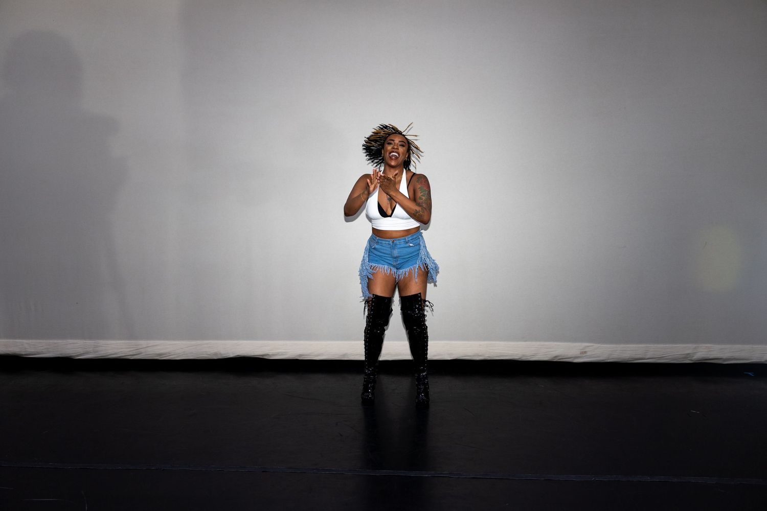 Dancer in white crop top and blue shorts performing on black stage floor.