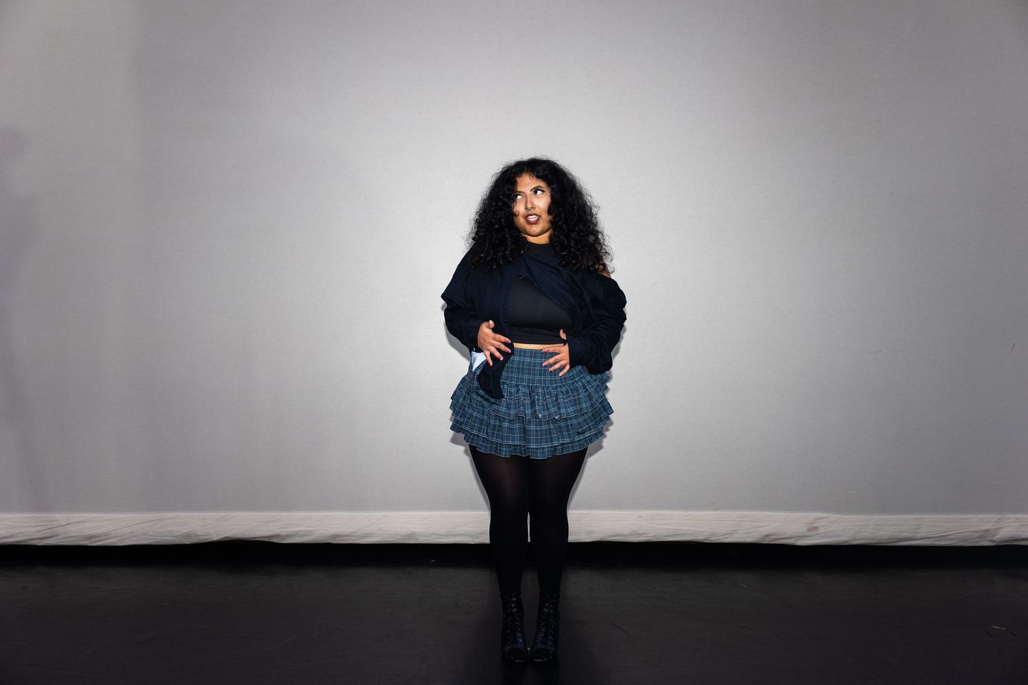 Woman in blue ruffled skirt and black jacket posing in a studio.