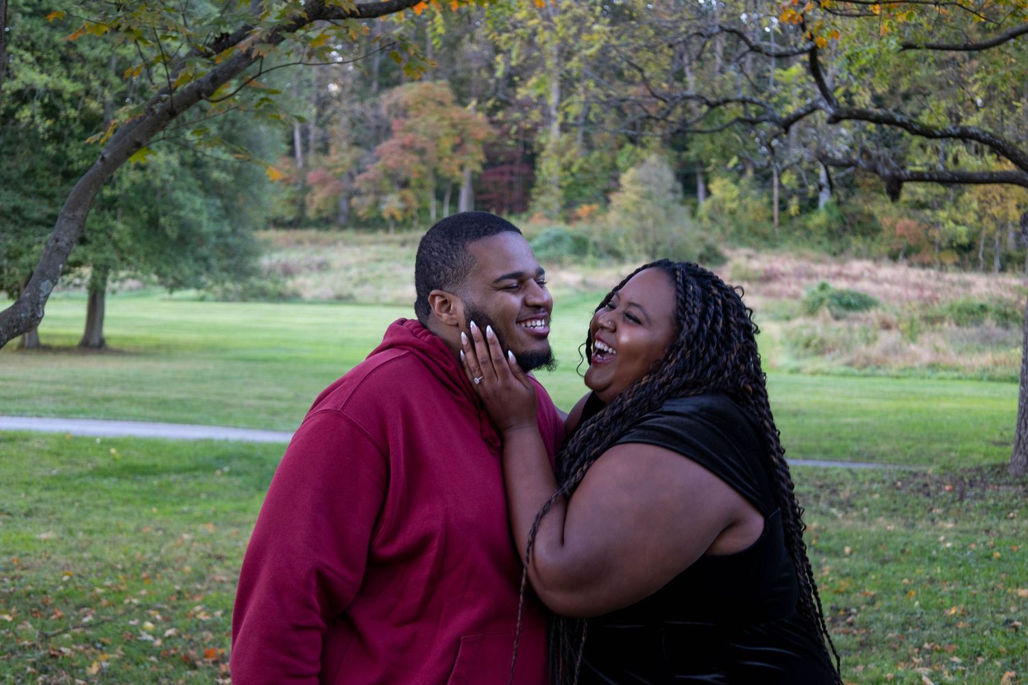 A joyful couple laughing together in a park during autumn, the woman tenderly holding the man's face.