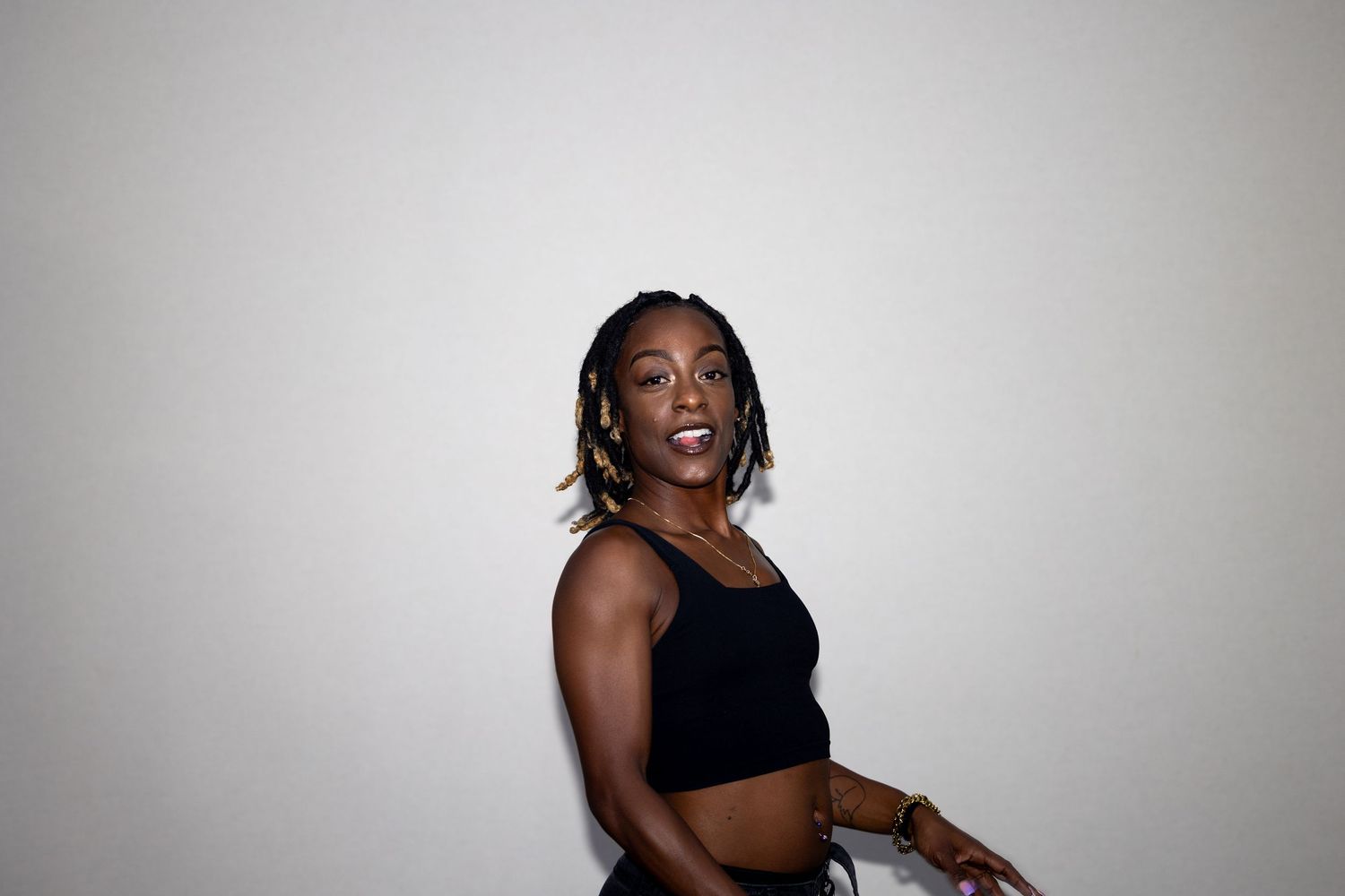 Athletic Black woman in black crop top dancing energetically against a white background.