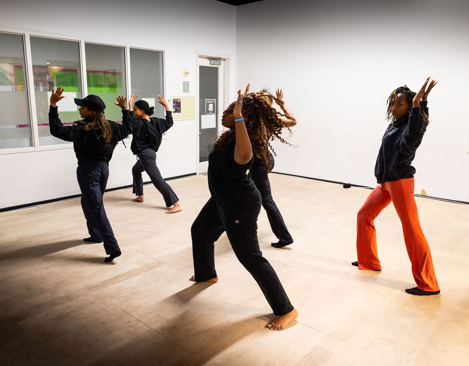 Four dancers rehearse dynamic contemporary moves in a bright studio with wood floors and white walls.