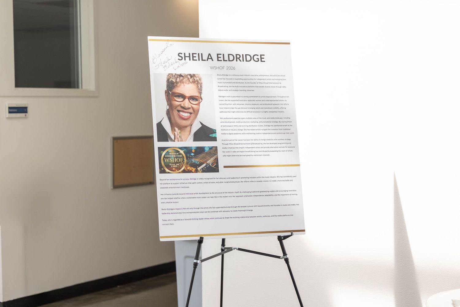 A poster on an easel honoring Sheila Eldridge with her photo and biography displayed in a bright room.