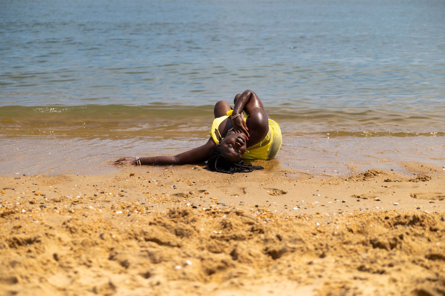 Person in yellow swimsuit lying on sandy beach shore with calm ocean waves in the background.