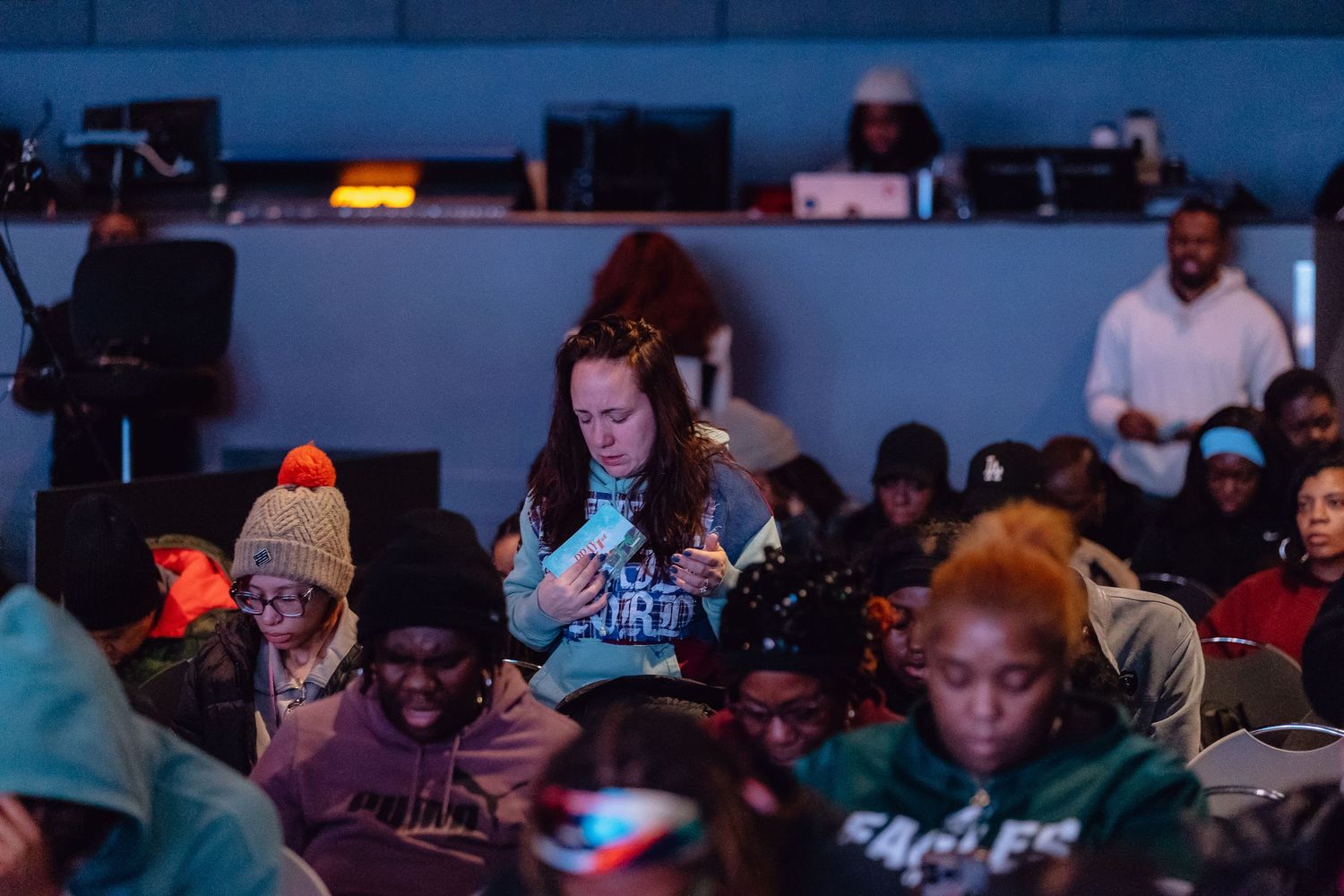 Diverse group of people working at computer stations in a dimly lit room with blue ambient lighting.