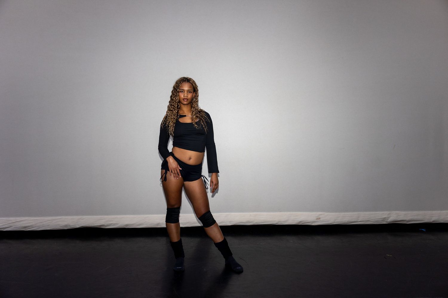 Woman in black crop top and shorts with knee-high boots posing confidently in a studio.