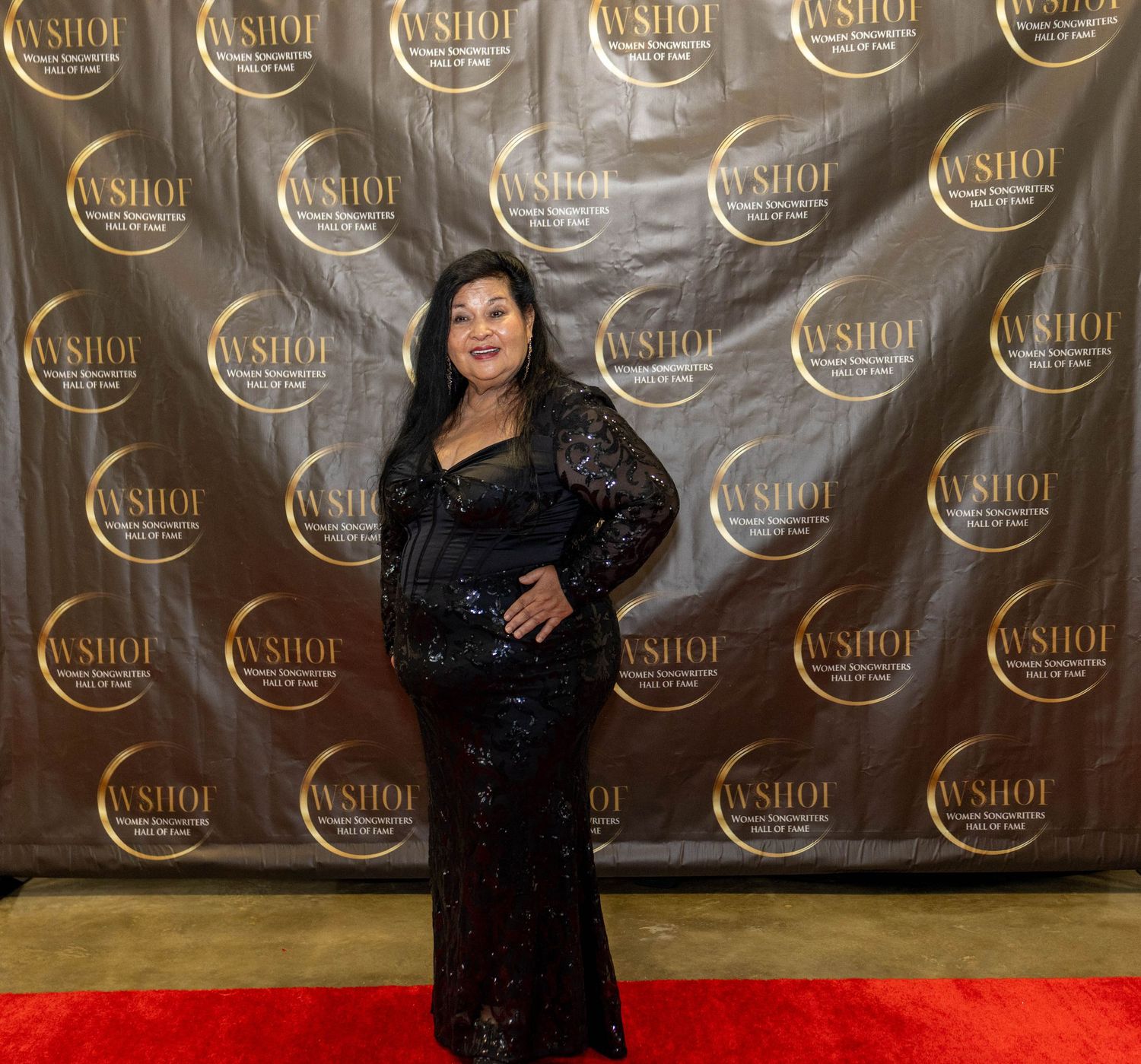 Woman in black sequin gown posing on red carpet at WSHOF awards event backdrop.