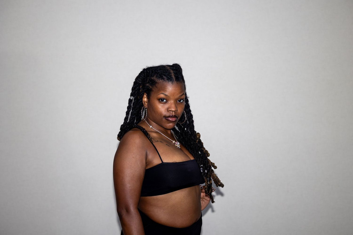 Black woman with long braids wearing a black crop top, posing confidently against a light background.