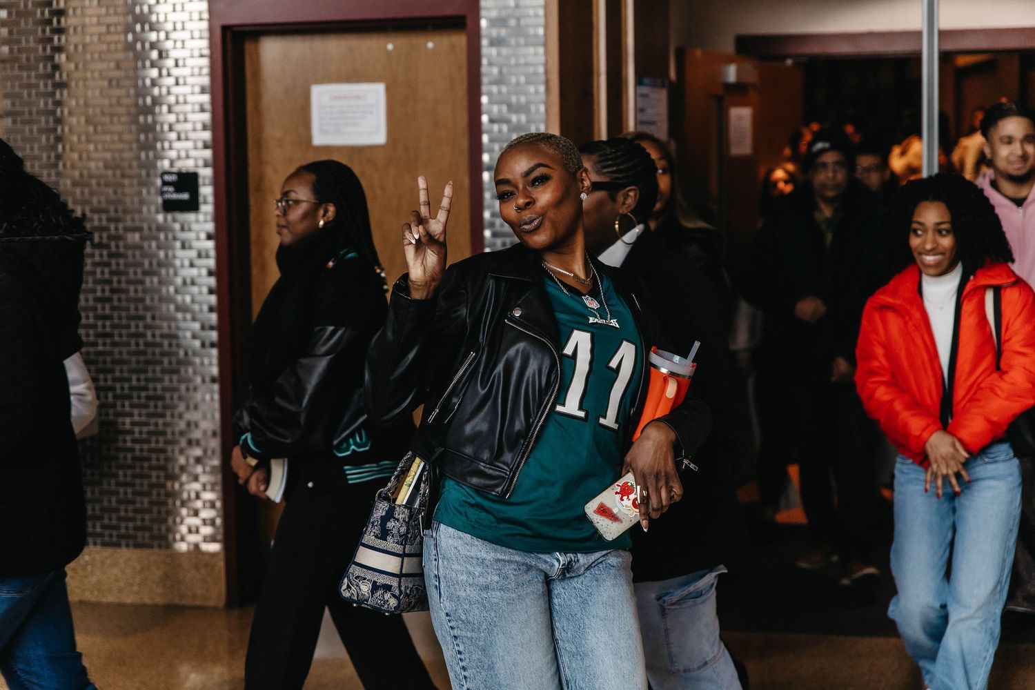 A group of people standing in a hallway with one person wearing a green jersey numbered 11 and another in a red jacket.