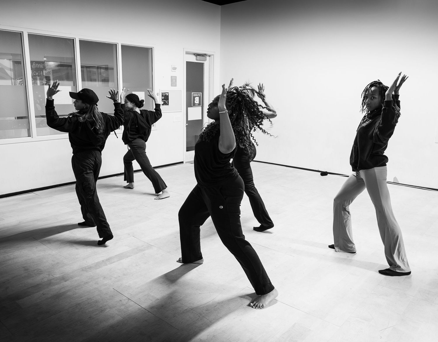 Black and white photo of four dancers performing dynamic moves in a bright studio space.