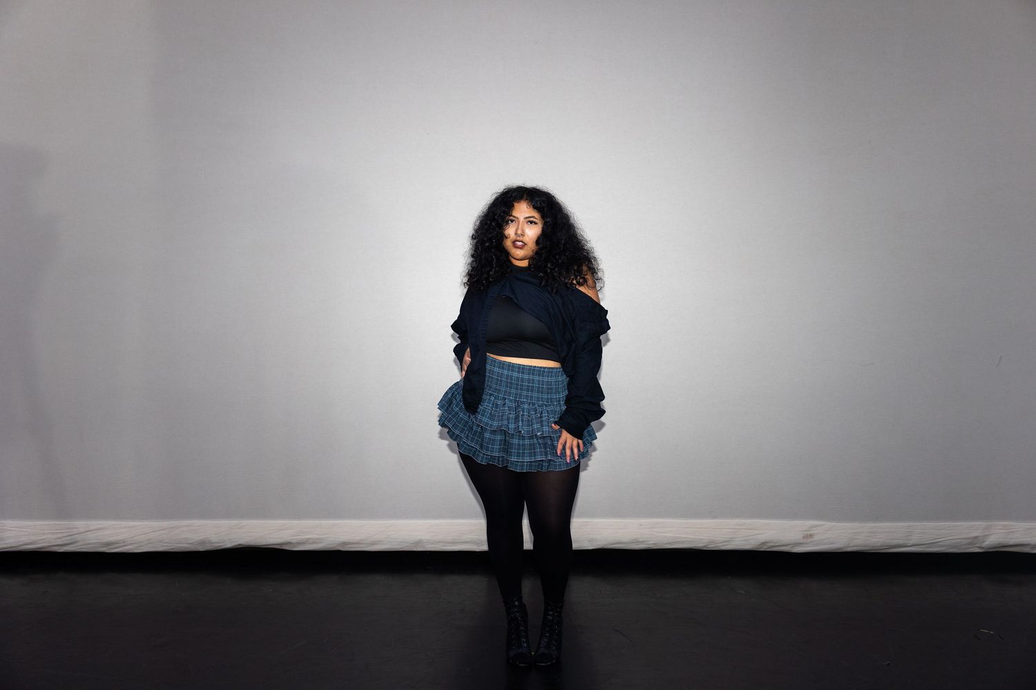 Woman in blue ruffled mini skirt and navy crop top standing confidently against a neutral gray background.