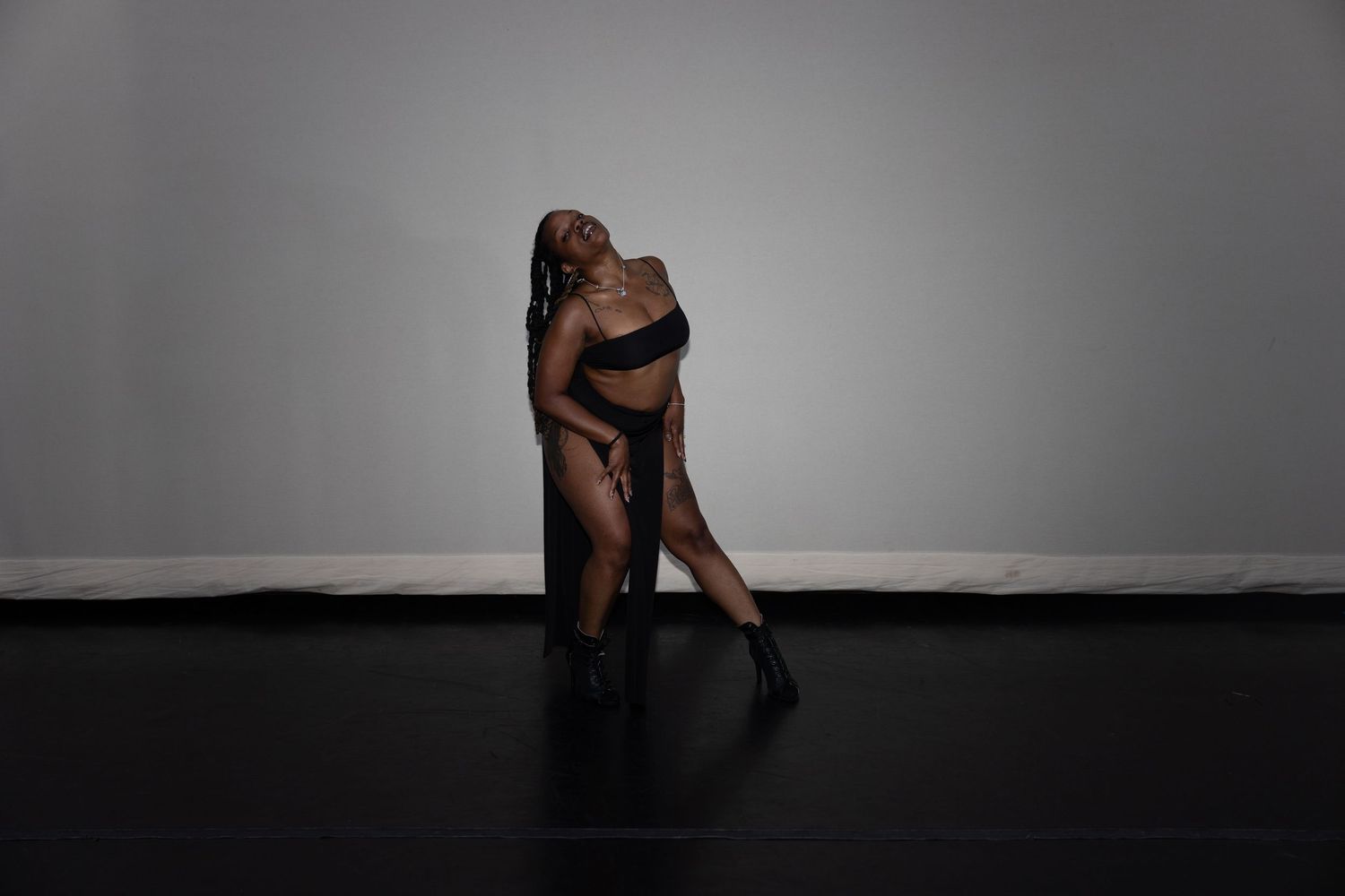 Woman in black lingerie posing dramatically in a dark studio.