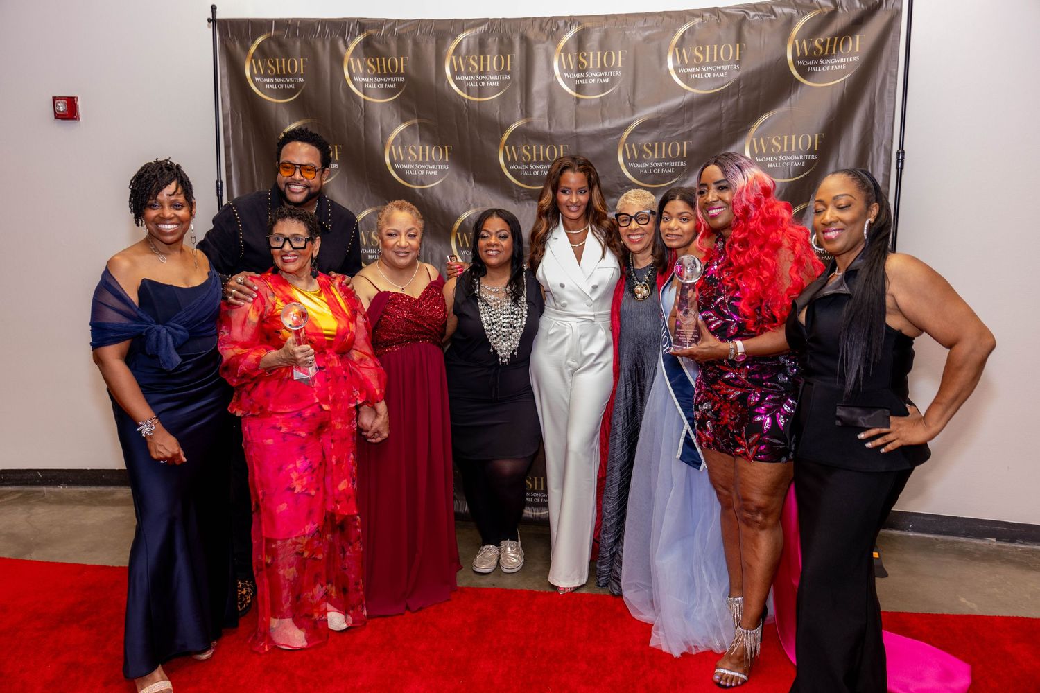 Group of elegantly dressed people posing together at a formal gala event in front of a branded backdrop.