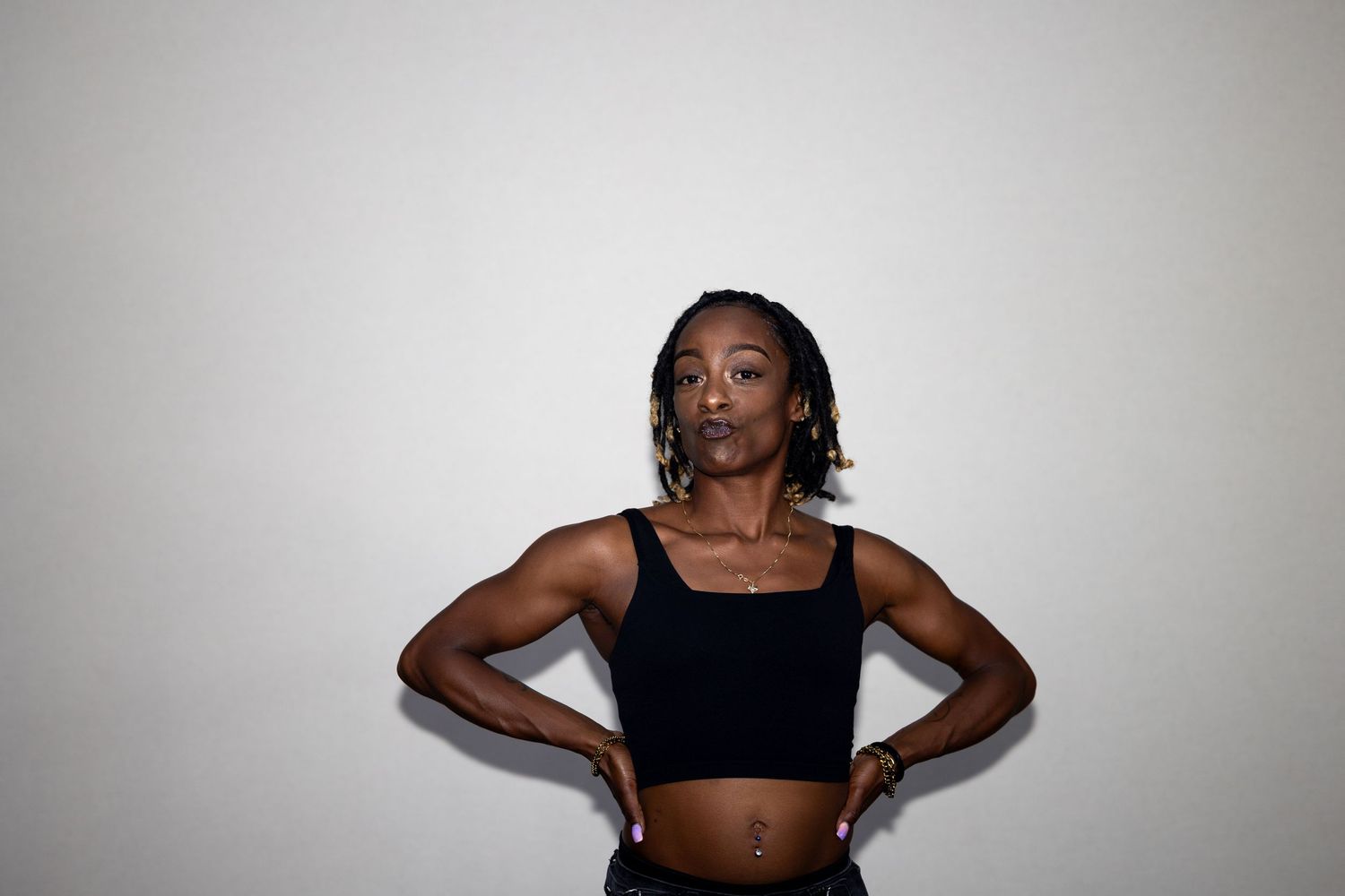 Athletic woman in black crop top stands with hands on hips against white background.