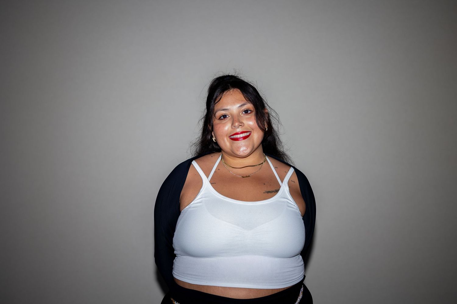 A plus-size woman in a white sports bra and navy cardigan smiles warmly against a gray background.