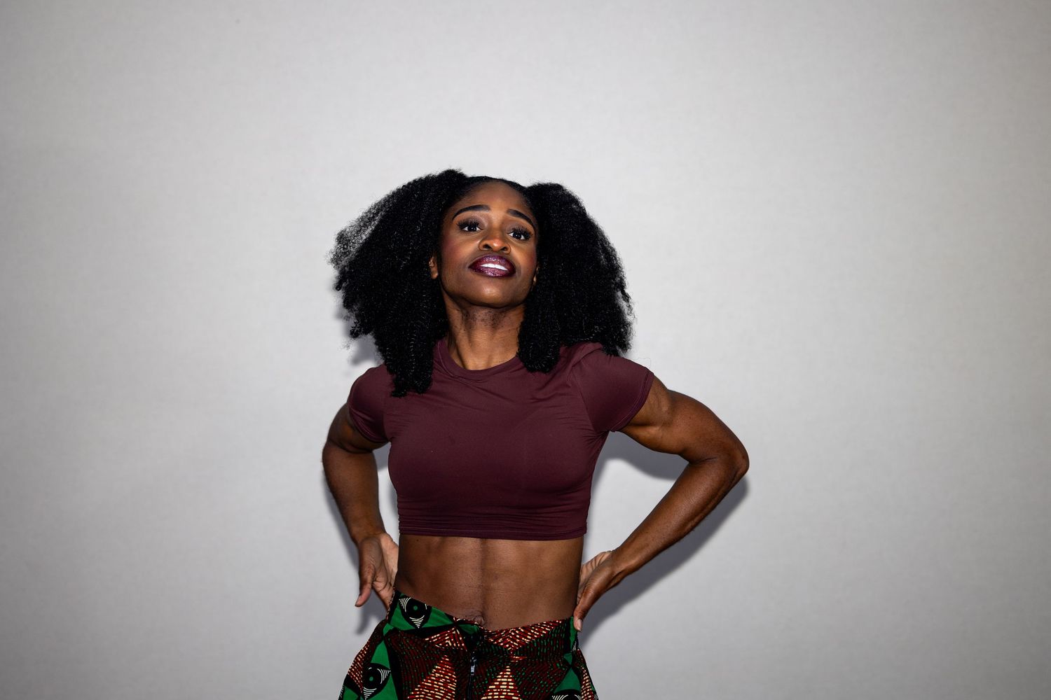 Young woman with natural afro in a maroon crop top and colorful skirt looking upward confidently.