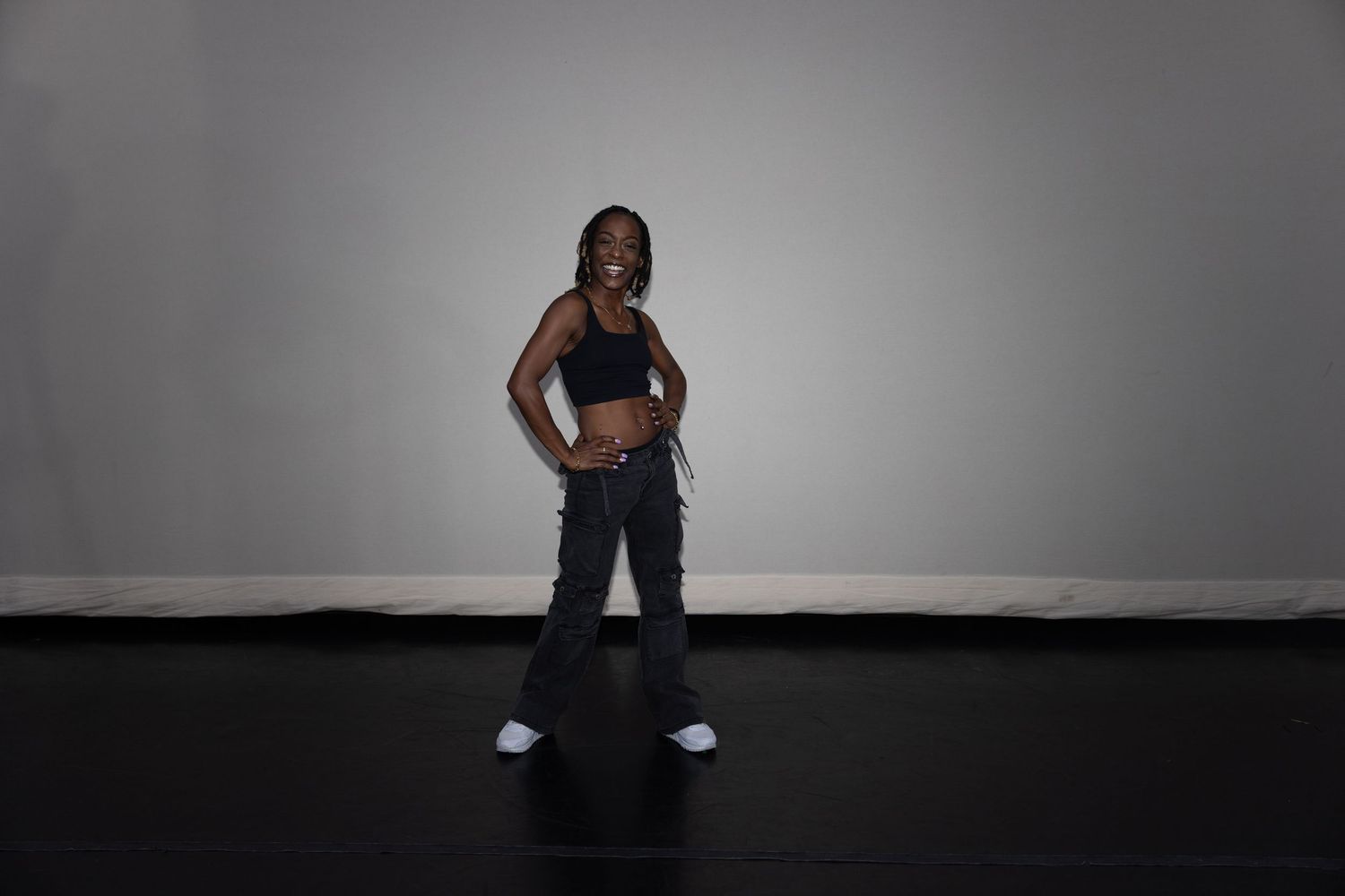 Woman in black sports bra and cargo pants posing confidently in a photography studio.