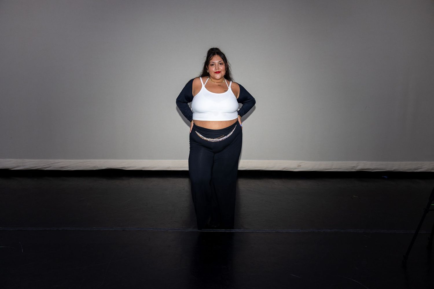 Plus-size woman in white crop top and navy wide-leg pants standing confidently against gray studio backdrop.