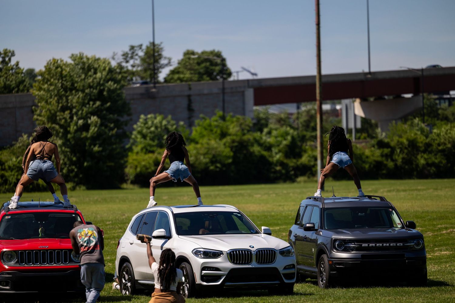 People dancing on top of SUVs including BMW and Jeep on a grassy field during an outdoor event.