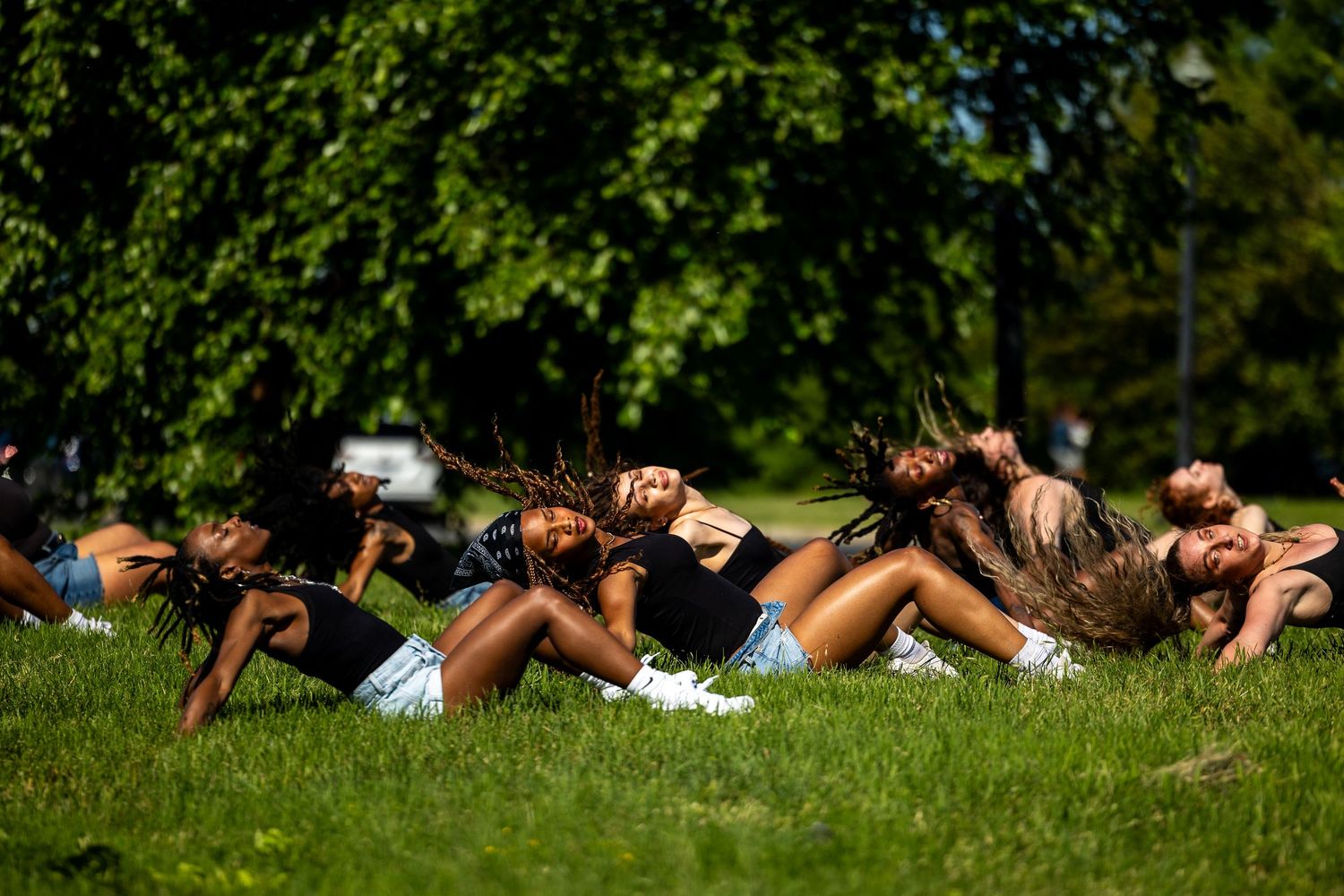 Girls lying on grass in a park, tossing their hair back in unison on a sunny day.