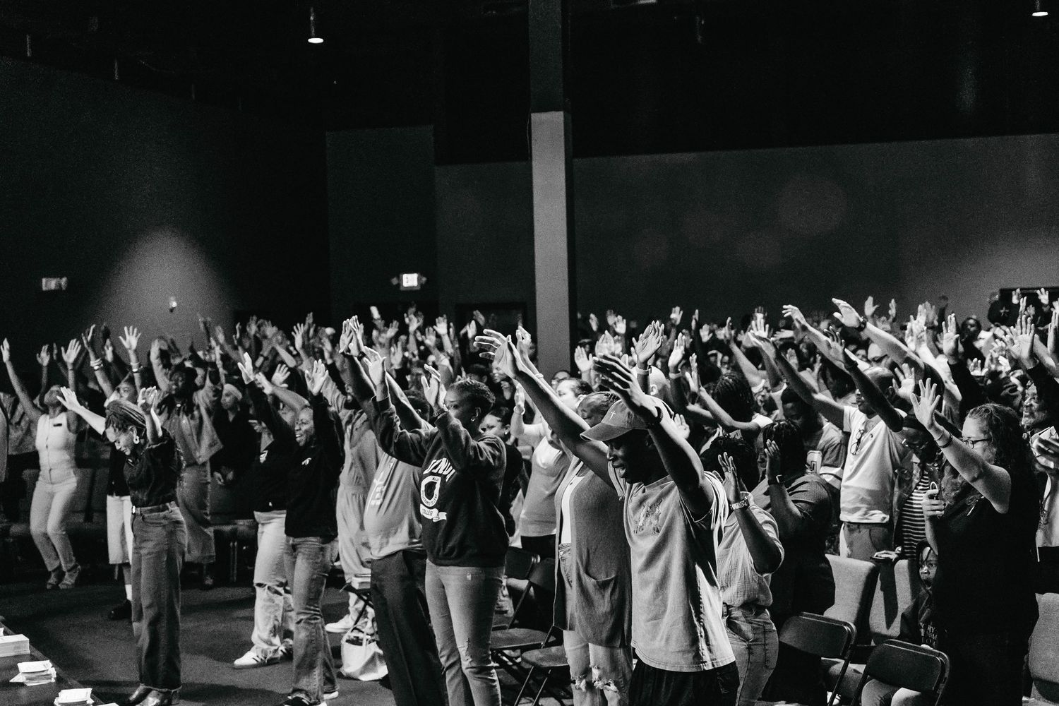 Large crowd with raised hands worshipping together in a dark indoor venue during a religious gathering.