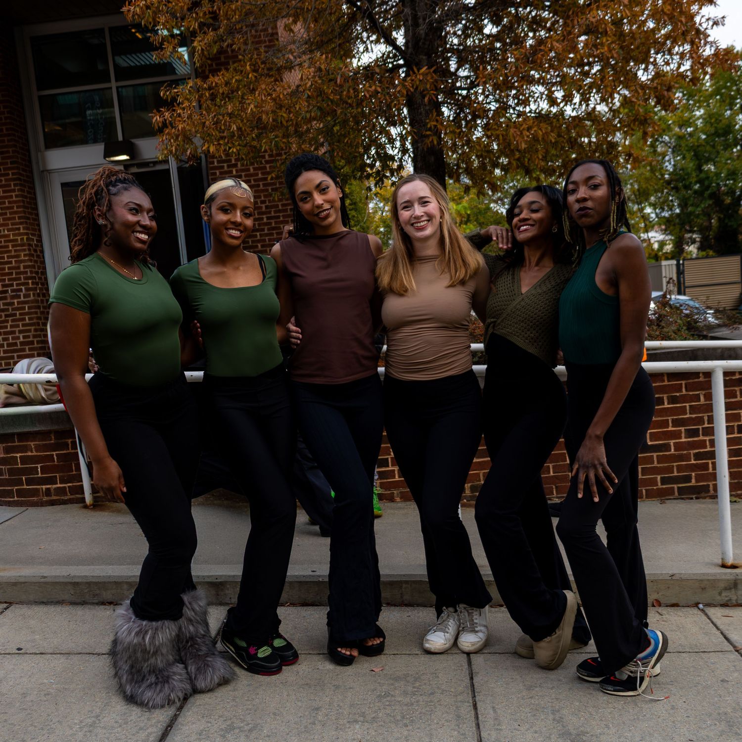 A group wearing coordinated brown and green outfits poses together on a brick walkway during autumn.