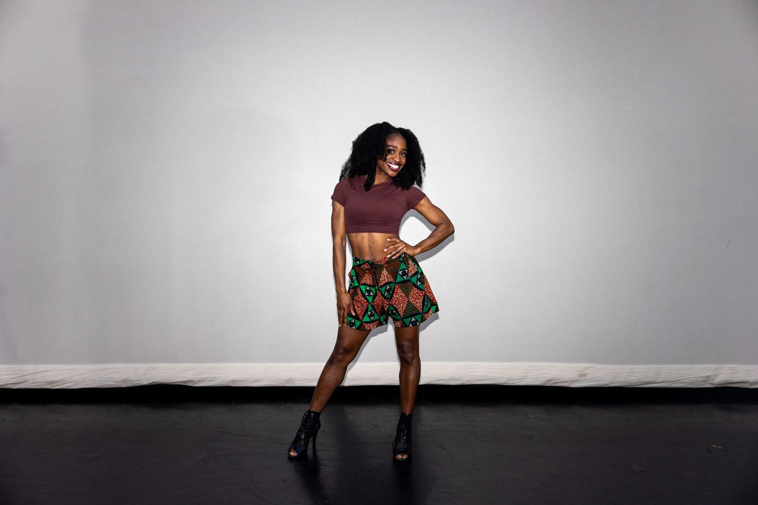 A woman in a colorful African print skirt and crop top poses in a studio.