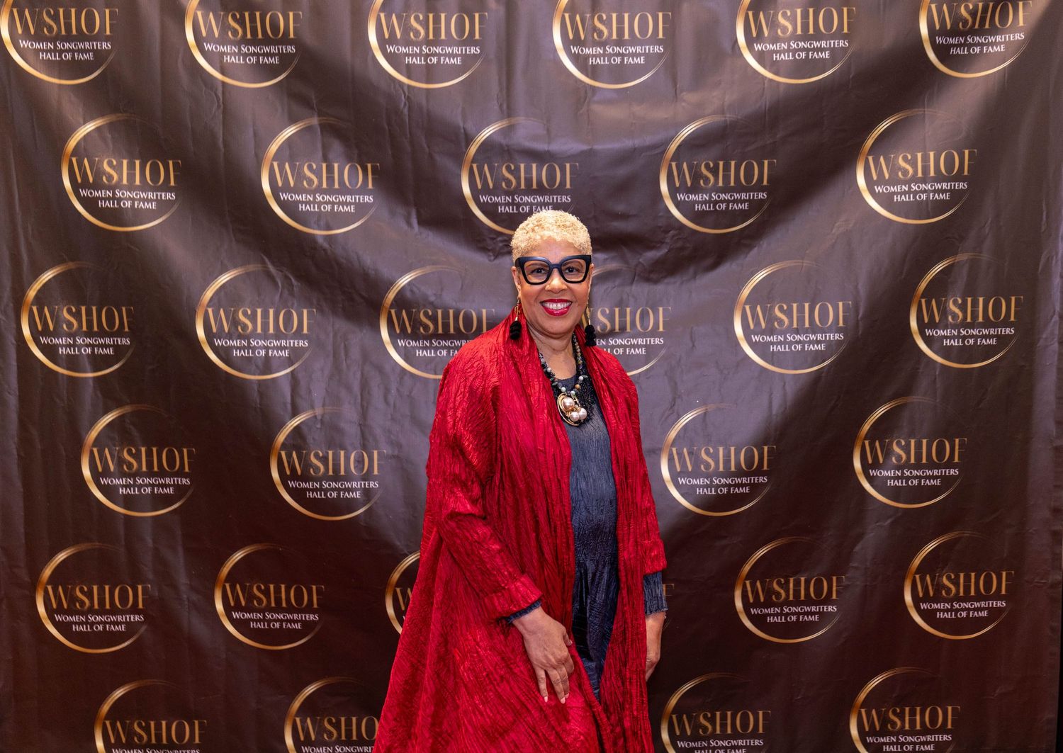 Woman in red kimono jacket poses at WSHOF awards event backdrop.