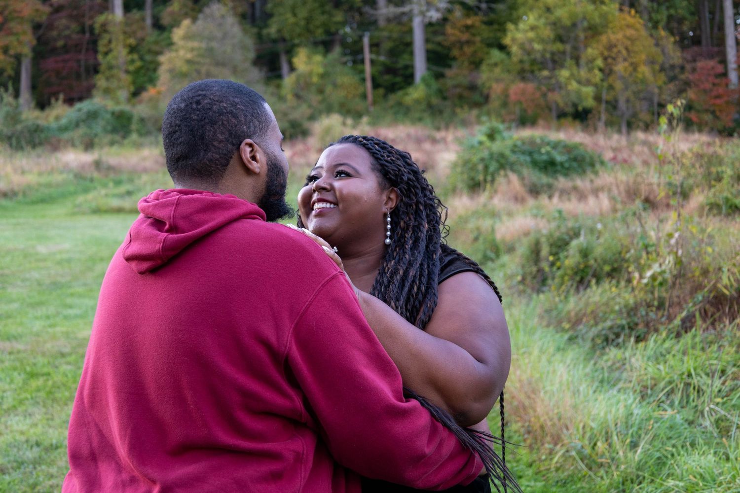 A joyful Black couple sharing a happy moment together in a lush green field with autumn foliage.