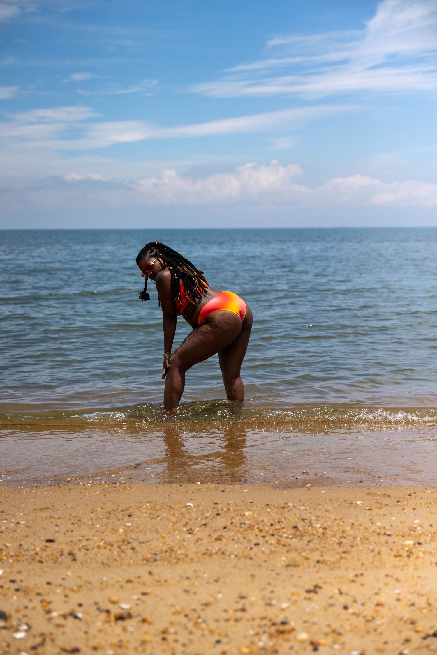 Woman in colorful swimsuit standing in shallow ocean water on a sandy beach under a blue sky.
