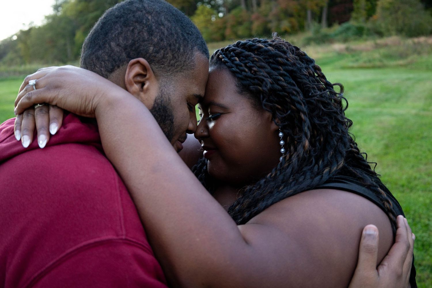 Engaged couple sharing an intimate nose-to-nose moment embracing outdoors in a green field.