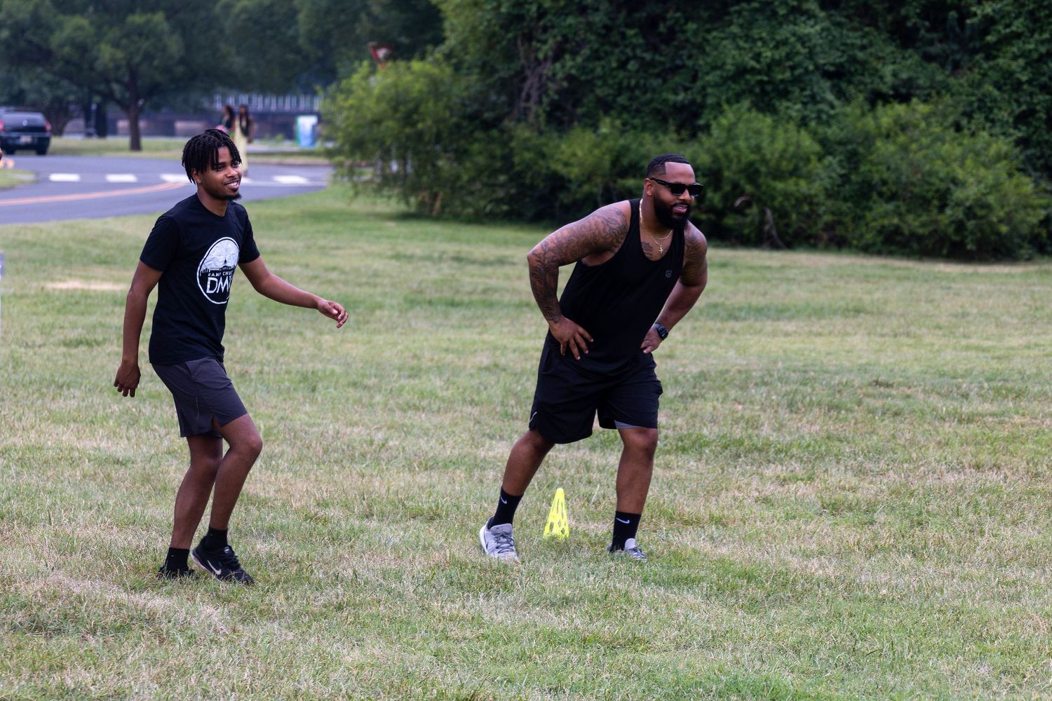Two men in athletic wear practice agility drills with cones on a grassy field outdoors.