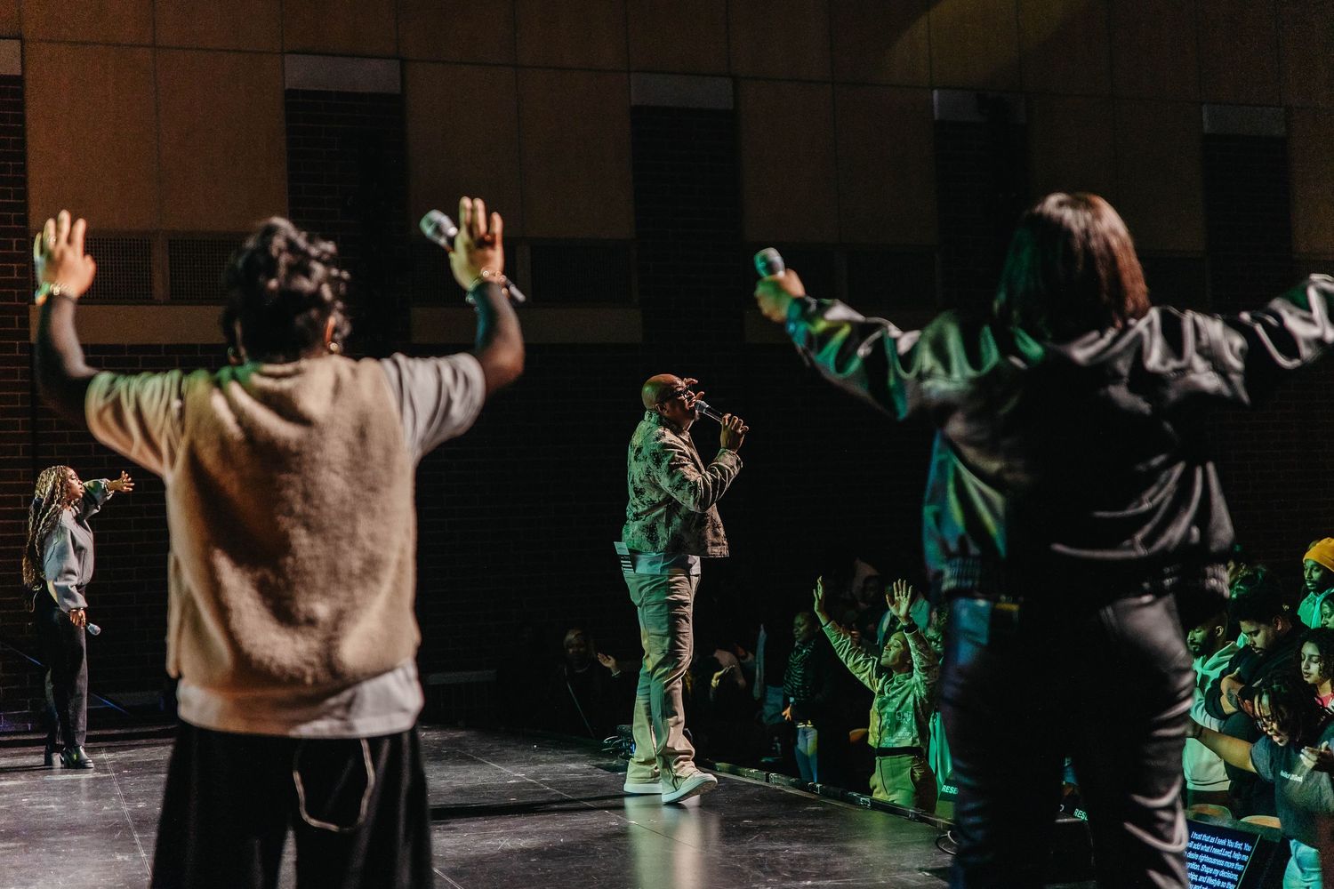 Silhouetted dancers perform dynamic movements on a dark stage with dramatic green lighting effects.