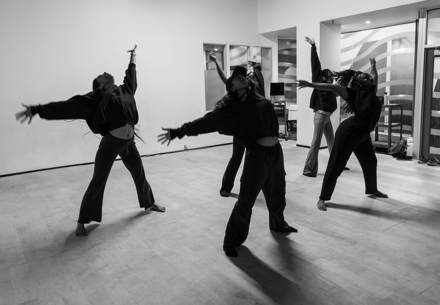 Black and white photo of dancers in dynamic poses wearing all black in a modern studio space.