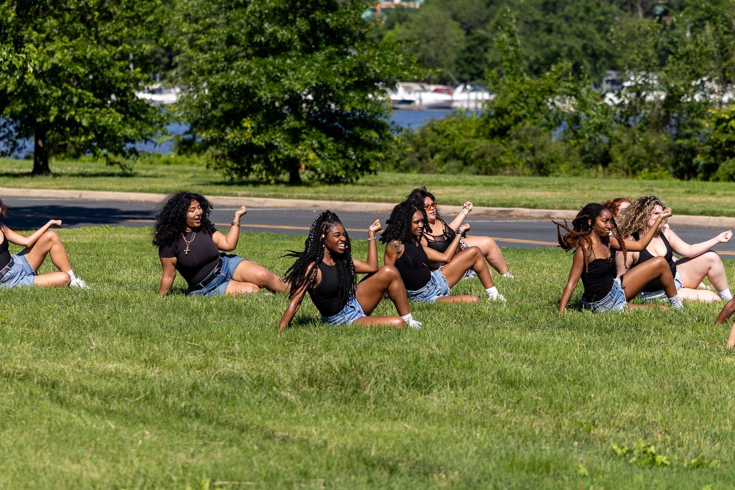 Group of young women sitting on a grassy hill outdoors, posing and smiling together.