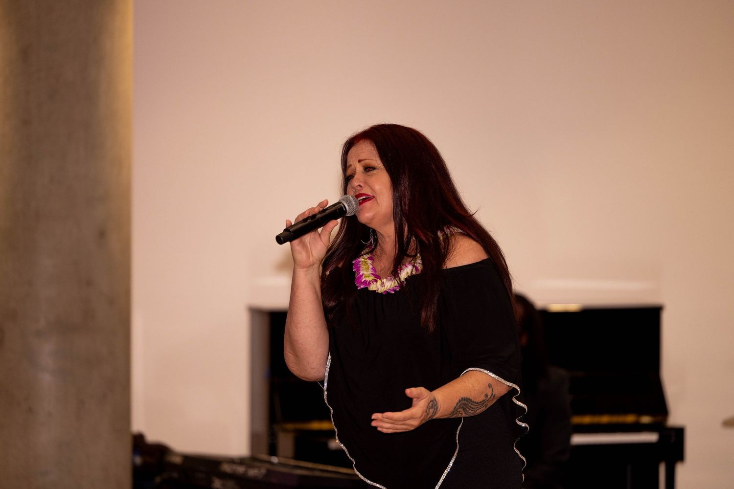 Woman with long dark hair sings into microphone on stage near a grand piano.