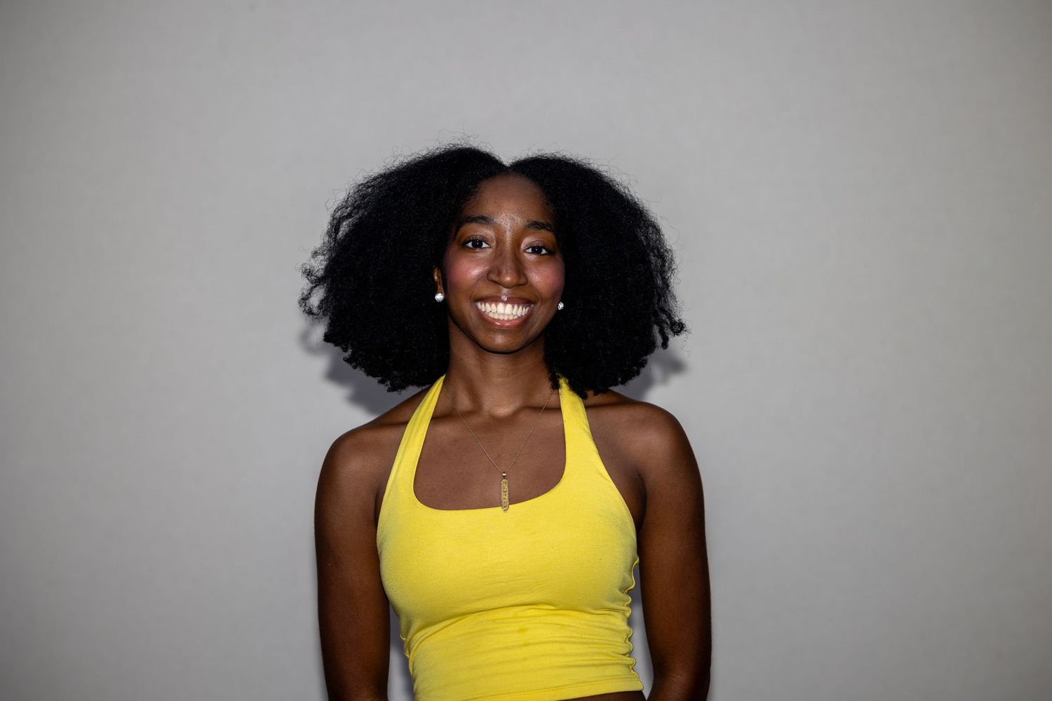 Smiling woman in yellow halter top with natural afro hair against gray background.